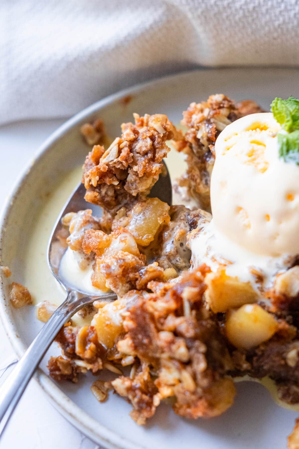 A spoon scooped of apple crips served with vanilla ice cream on a plate. 