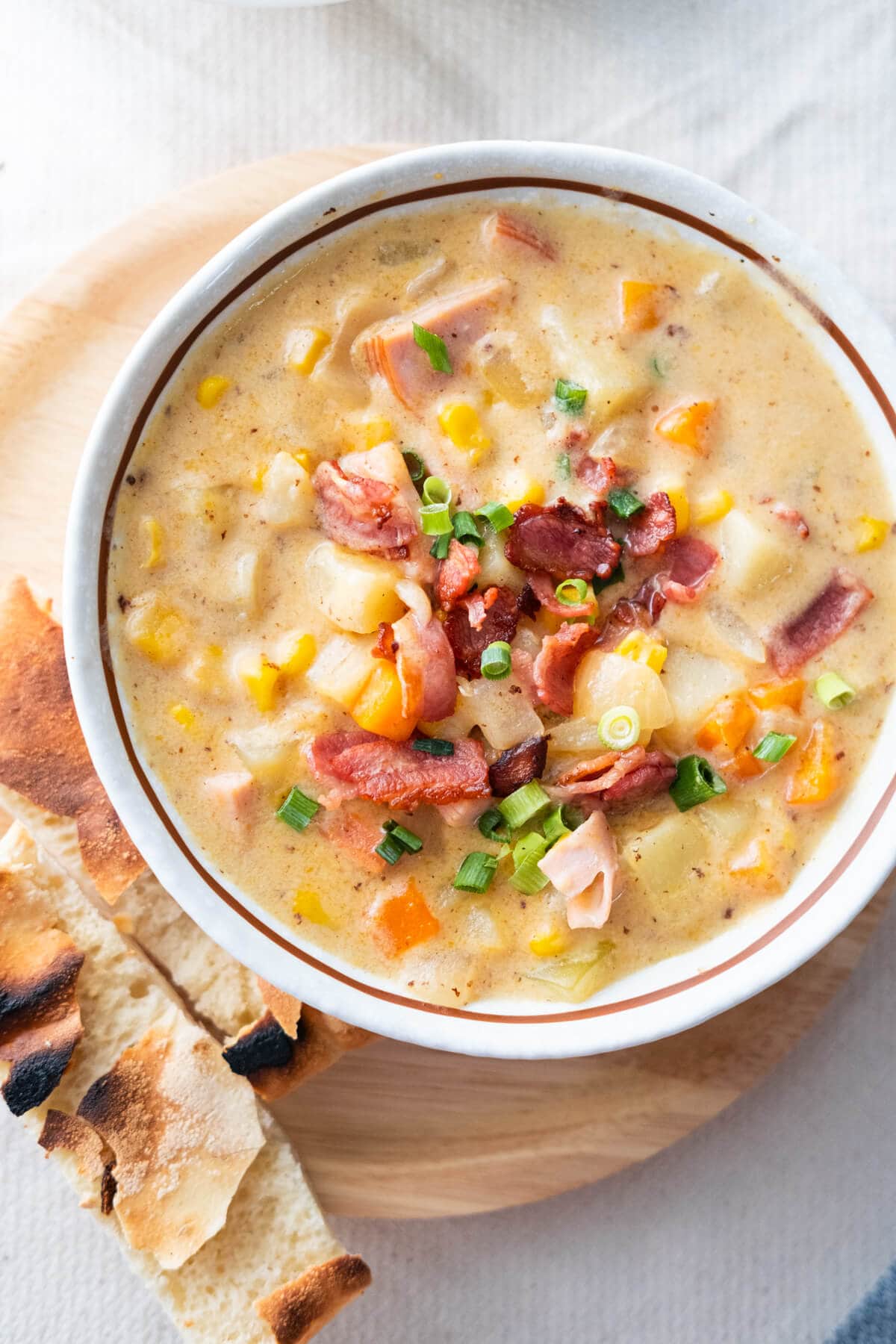 Creamy cheesy ham chowder filled with vegetables, ham, cheddar cheese and crisp bacon served in a bowl with bread at the side. 