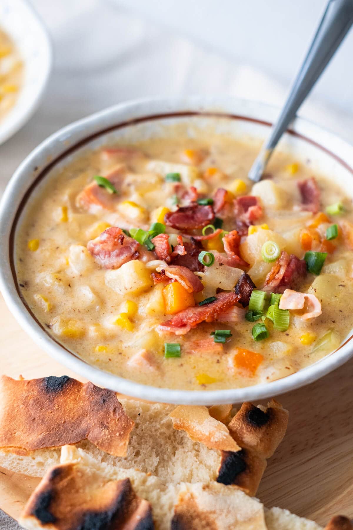 Chowder with potato cubes, carrots, corns, ham and bacon served in a bowl and spoon. 