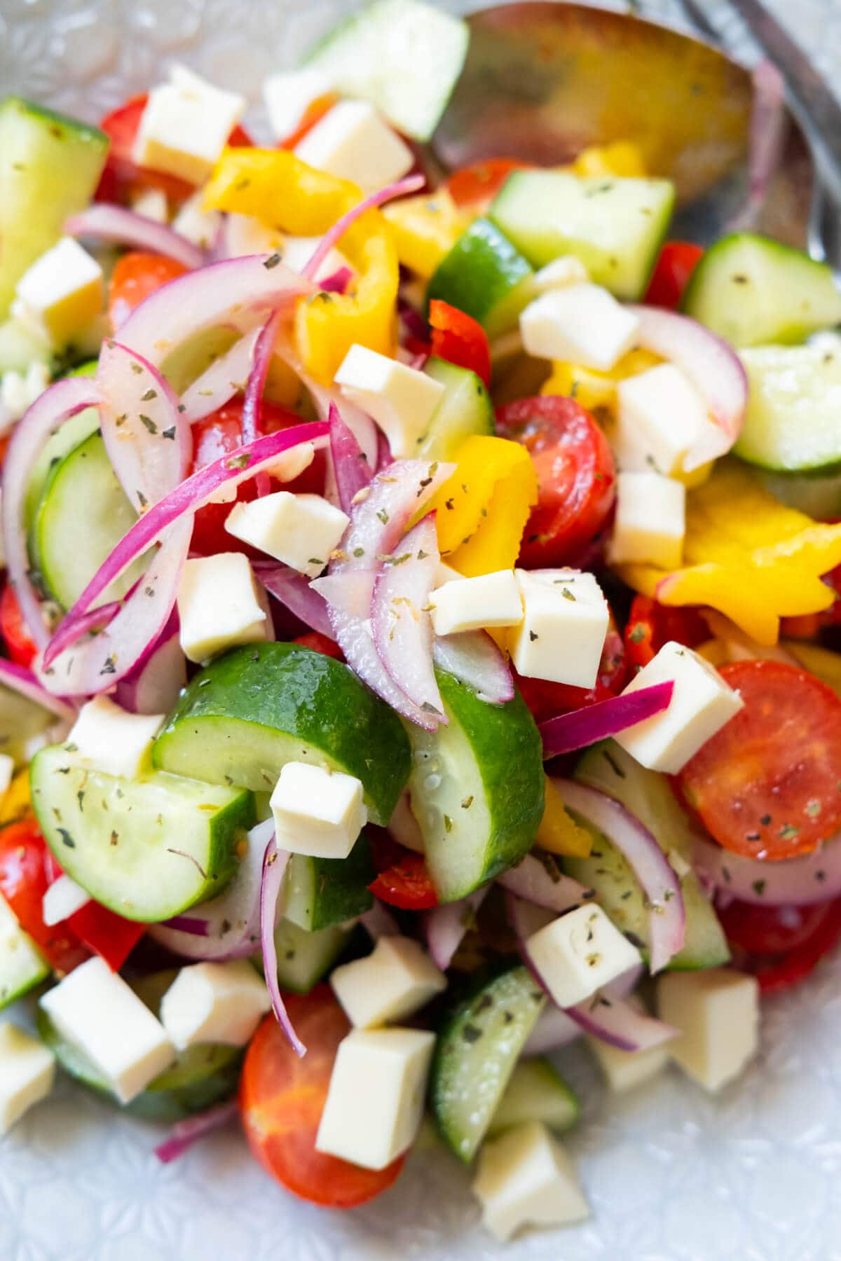 Closed up shot of fresh delicious salad consists of red onion, cherry tomatoes, yellow bell pepper, red bell pepper, cucumber, and feta cheese. 